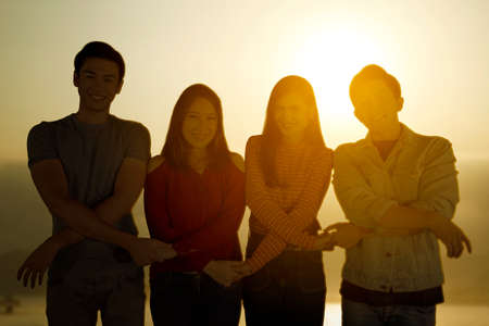 Group of young people holding hands each other while standing on the beach with sunset backgroundの写真素材