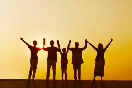 Silhouette of happy three generation family standing together with raised hands on the hill. Shot at sunset timeの写真素材