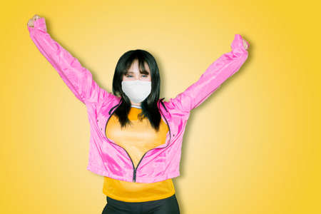 Female dancer wearing face mask while performing dance in the studio with yellow background