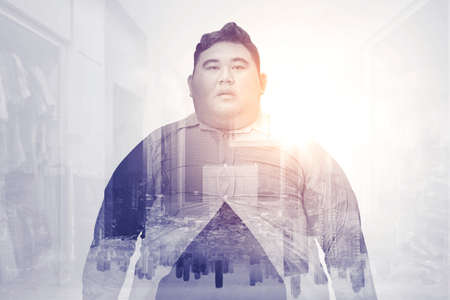Double exposure of fat young man wearing tight unbuttoned shirt while standing with cityscape backgroundの写真素材