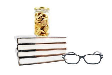 Close up of glass jar full of Cryptocurrency coins with pile of books and glasses. Isolated on white backgroundの写真素材