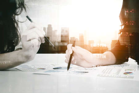Double exposure of two businesswomen discussing with a business finance chart on paper in cityscape...
