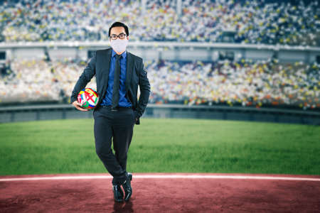 Picture of businessman wearing face mask while holding a ball with european flags for football tournament and standing in the stadiumの写真素材