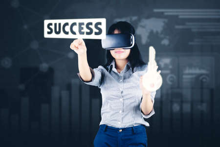 Young businesswoman using a VR glasses to touching success word and key symbol while standing with...