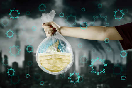 Hand holding globe wear face mask in plastic bag with coronavirus and polluted city background