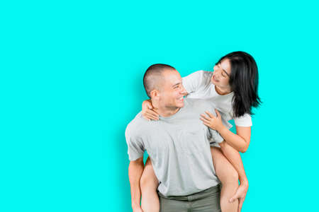 Happy young couple playing a piggyback ride while standing with copy space in the studioの写真素材
