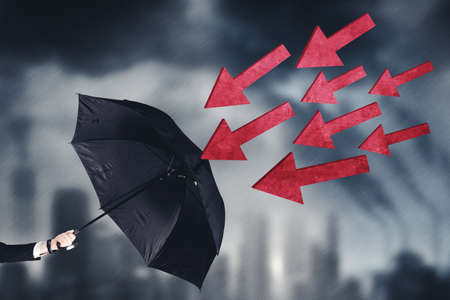 Close up of businessman hand holding an umbrella while protecting from attacking arrow in gloomy city backgroundの写真素材