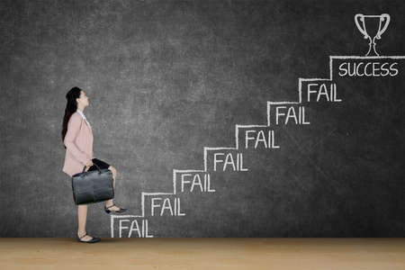 Side view of businesswoman carrying a suitcase while climbing stairs with fail word toward success word with trophyの写真素材