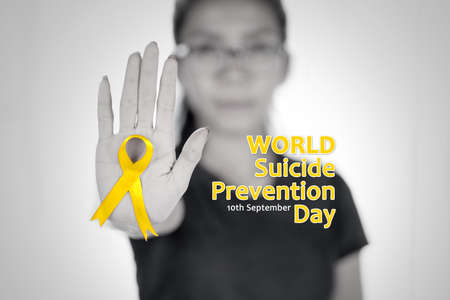 Close up of young woman showing a yellow ribbon and hand gesture to stop while standing with World Suicide Prevention Day textの写真素材