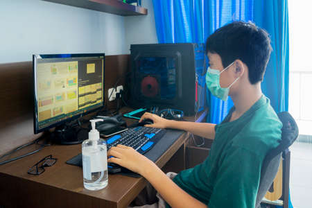 Preteen boy wearing a face mask while using a computer laptop and studying from home during self isolation at homeの写真素材