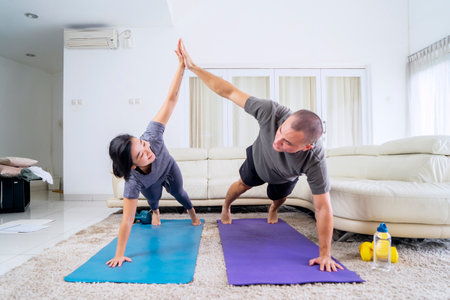 Young couple making high five hand gesture while doing plank exercises in the living room. Shot at...