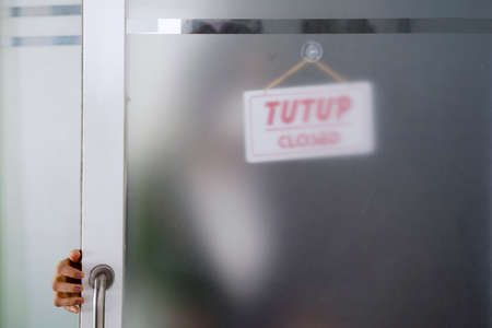 Young businesswoman putting a store sign with closed word on a storefront while impacted by...