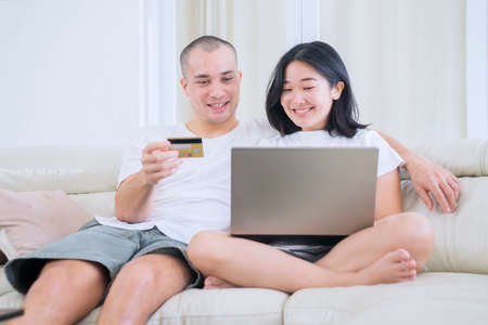 Happy young couple shopping online by using a laptop while sitting on the couch. Shot at home