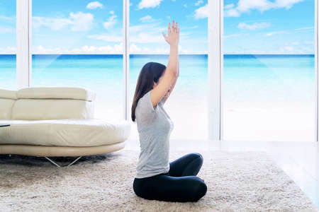 Side view of young woman lifting hands while doing yoga exercise in the resort with beach scenery backgroundの写真素材