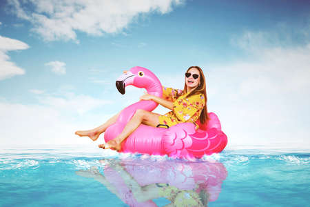 Happy young woman with flamingo inflatable float in tropical beach with blue sky background