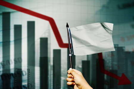 Double exposure of businessman hand rise white flag and give up with declining arrow in cityscape backgroundの写真素材