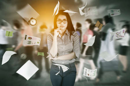 Thoughtful businesswoman thinking idea while standing with flying papers and crowded people...