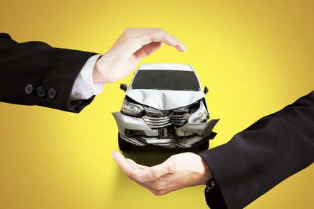 Insurance concept. Close up of businessman hands protecting a broken car with yellow backgroundの写真素材