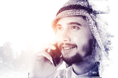 Double exposure of Arabian man talking on the cellphone while standing with cityscape backgroundの写真素材