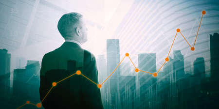Rear view of caucasian businessman looking at increasing finance graph with double exposure of skyscraper backgroundの写真素材