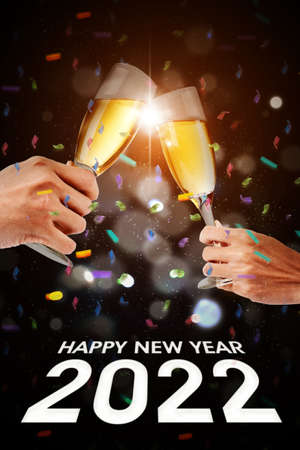 Young couple hands toasting with champagne under falling confetti with happy new year 2022 text in dark backgroundの写真素材