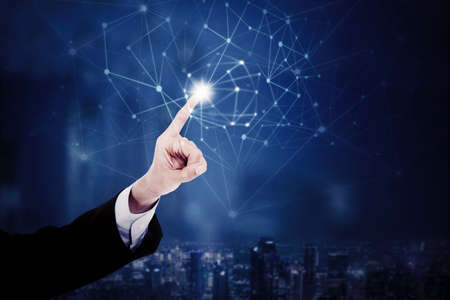 Close up of male manager hand touching network connection lines on virtual screen with night city backgroundの写真素材