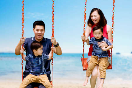 Image of happy parents playing swings with their sons while doing vacation in the tropical beachの写真素材