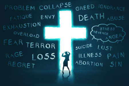 Silhouette of depressed young woman standing in front of the bright Cross symbol with problem...