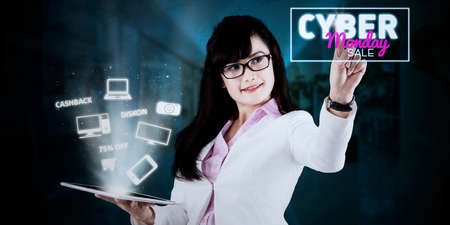 Young businesswoman showing electronic device on the tablet while touching cyber monday sale text on the virtual screenの写真素材