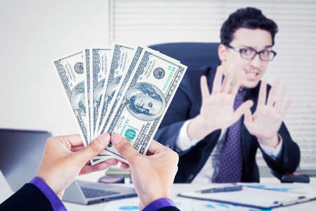 Refusing bribe concept. Young businessman refusing bribe money while sitting in the office