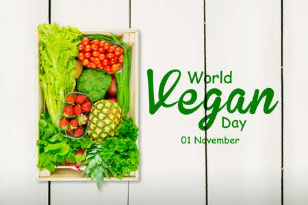 Variety of vegetables and fruits in wooden box with world vegan day text above the tableの写真素材