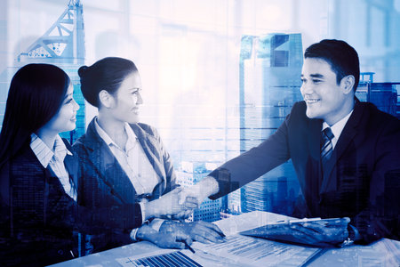 Double exposure of happy business people handshaking after business meeting while sitting with office buildings backgroundの写真素材