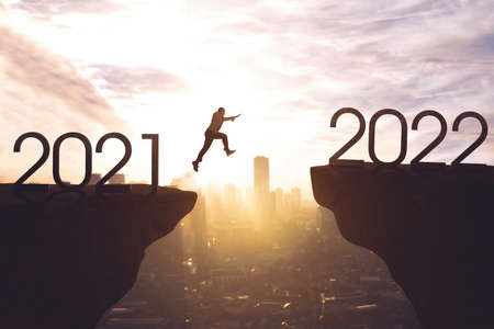Male entrepreneur jumping through gap from 2021 numbers to 2022 numbers with cityscape background. Shot at dawn timeの写真素材