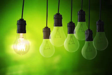 Close up of bright hanging light bulb with off bulbs in blurred green lights background