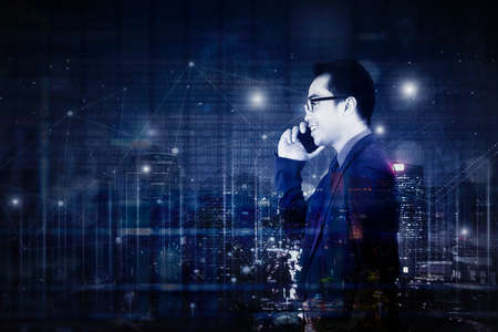 Double exposure of male manager makes a calling phone while standing with connection network lines and night city backgroundの写真素材