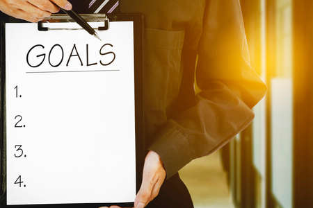 Close up of young businessman hands showing goals list on the clipboard while standing in the office corridorの写真素材