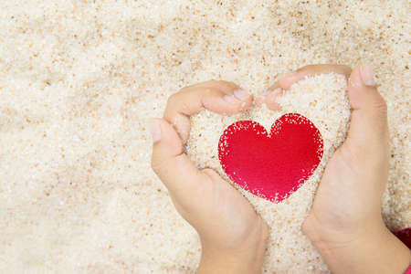 Close up of man hands holding sand while showing red heart symbol in the beachの写真素材