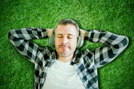 Top view of Caucasian man listening a music with headset while lying on the green grass. Shot at the parkの写真素材