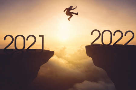 Male manager jumping gap on the cliff from 2021 numbers to 2022 numbers with misty morning backgroundの写真素材