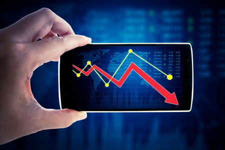 Close up of hand showing declining finance graph on cellphone screen with virtual screen backgroundの写真素材