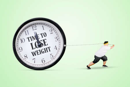 Young fat man using chains to pulling a clock with text of time to lose weight in the studioの写真素材