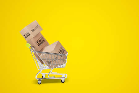 Image of trolley carrying full of packages with cash on delivery service in the studio with yellow backgroundの写真素材