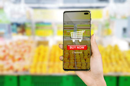 Young woman hand using a mobile phone apps to buying fresh fruits with supermarket background