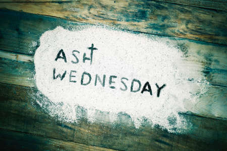 Close up of Ash Wednesday text written on the sand with wooden table backgroundの写真素材