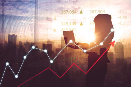 Silhouette of young businesswoman using a laptop while standing with double exposure of growth chart...