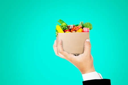 Close up of businessman hand gripping a bag full of groceries in the studio with tosca background