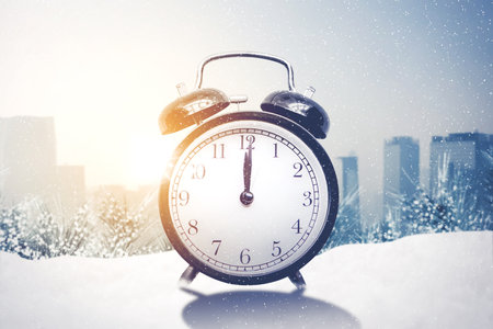 Close up of alarm clock on the snowy park with cityscape background. Shot at winter time