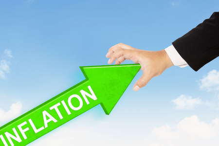 Close up of businessman hand try to hold back an upward arrow of inflation with cloudscape backgroundの写真素材