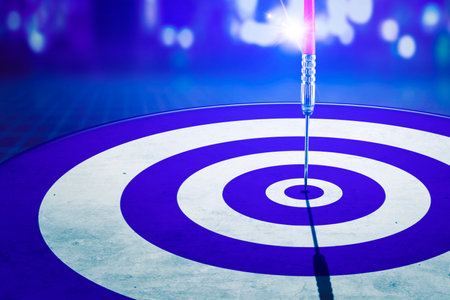 Close up of a dart on center of dartboard with blurred sparkling lights background. Shot in the...