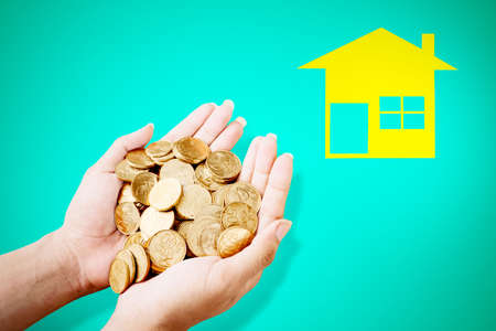 Close up of young man hands holding stacks of gold coins near the cardboard by house. C